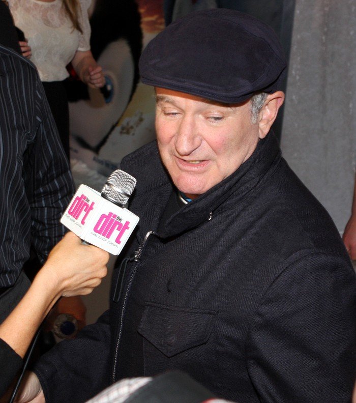 Robin Williams wearing a dark cap and coat while being interviewed at the Happy Feet Two premiere in Sydney in 2011