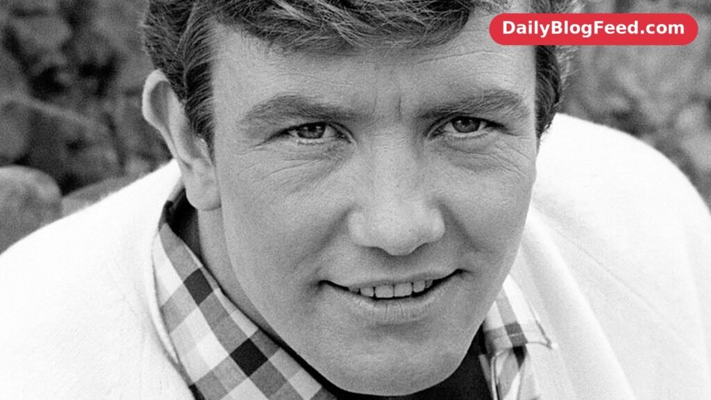 Albert Finney in a portrait from 1966, smiling in a checked shirt and light cardigan
