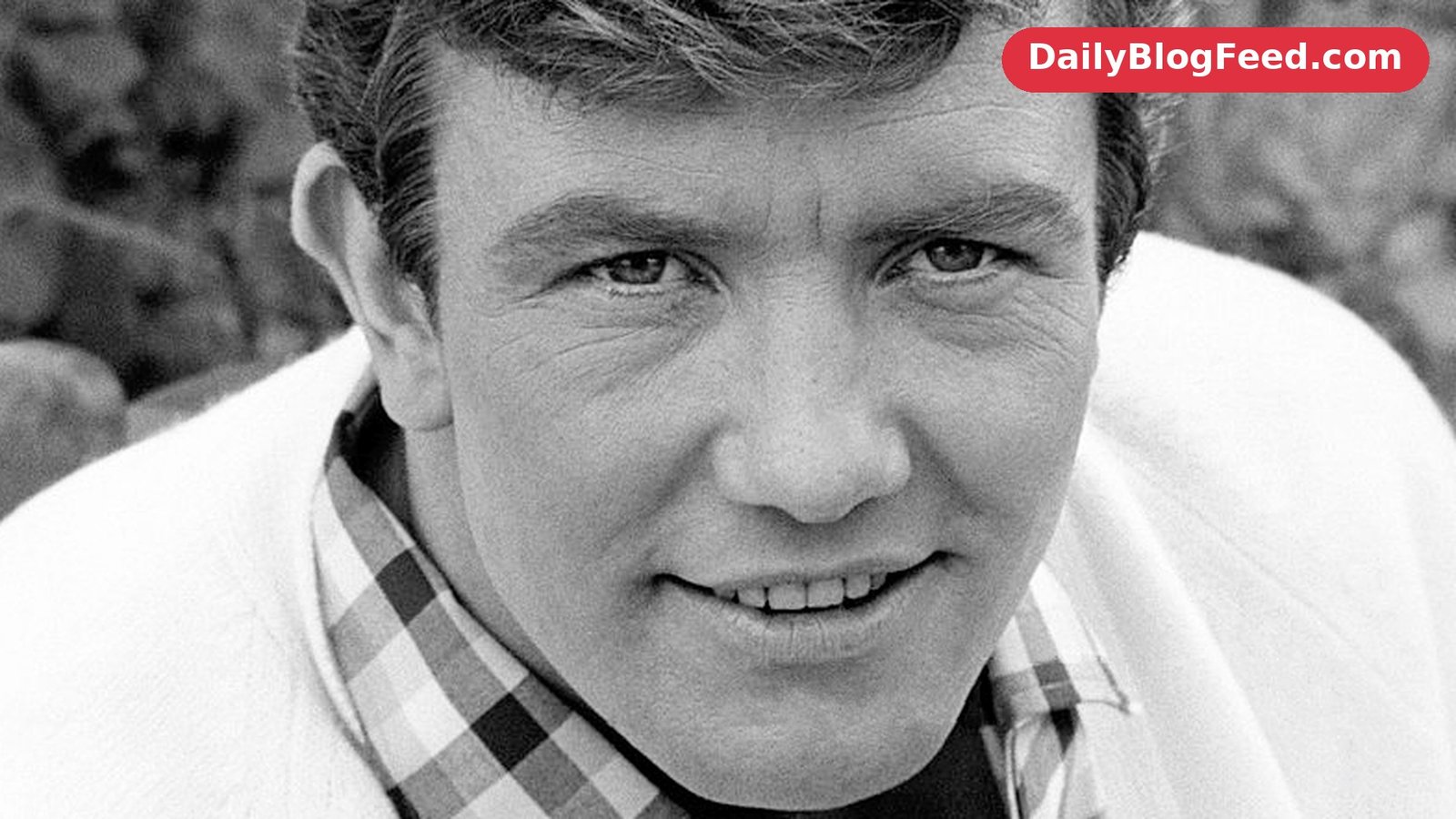 Albert Finney in a portrait from 1966, smiling in a checked shirt and light cardigan