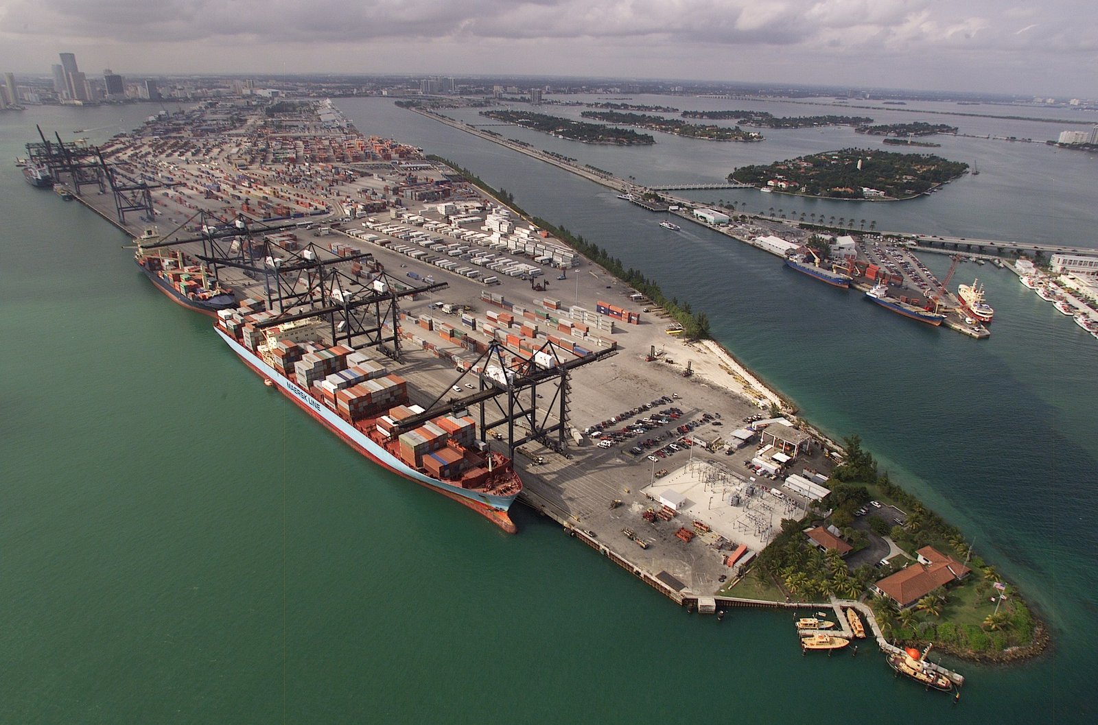 Aerial photograph of a container port with stacked shipping containers and cargo cranes beside the water