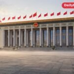 Grand columned government hall in Beijing with red flags in front and a wide empty plaza in morning light